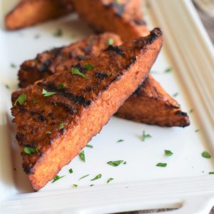 two pieces of grilled tempeh steaks on a white platter with some blurred out behind them