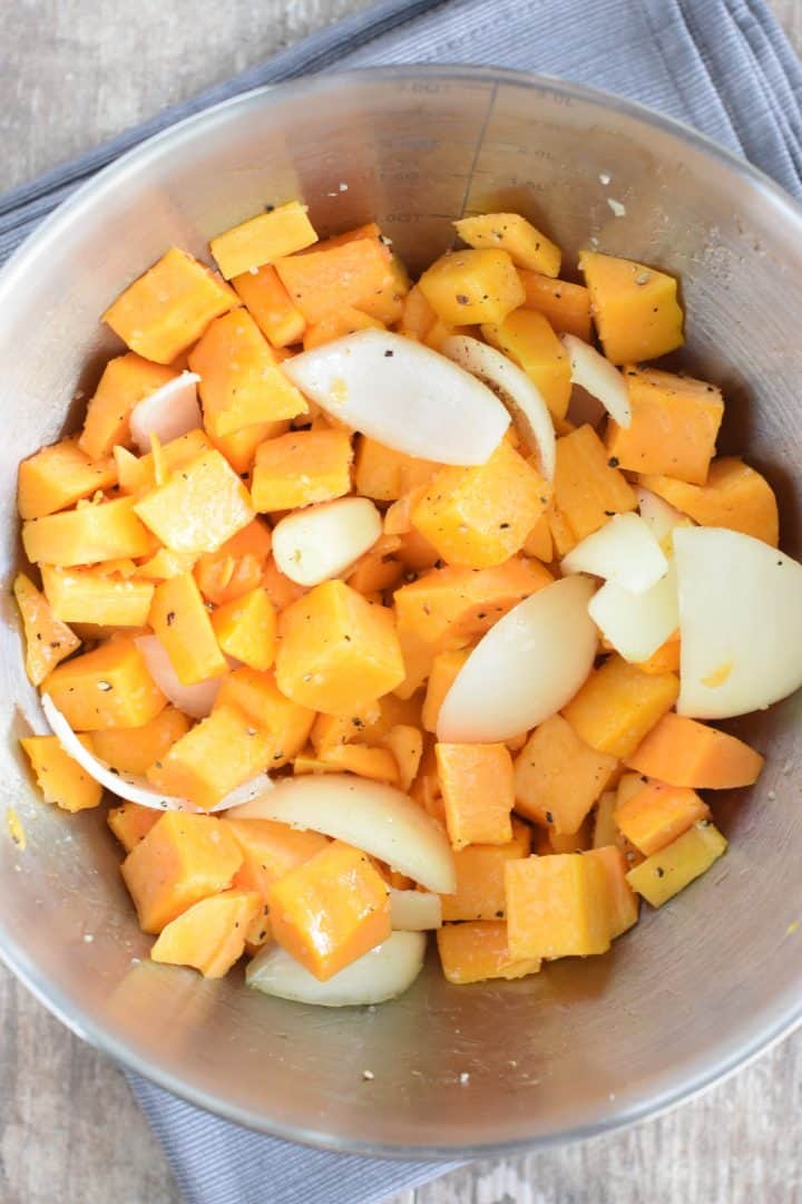 Butternut squash chunks, onion and garlic in a mixing bowl with olive oil, salt and pepper