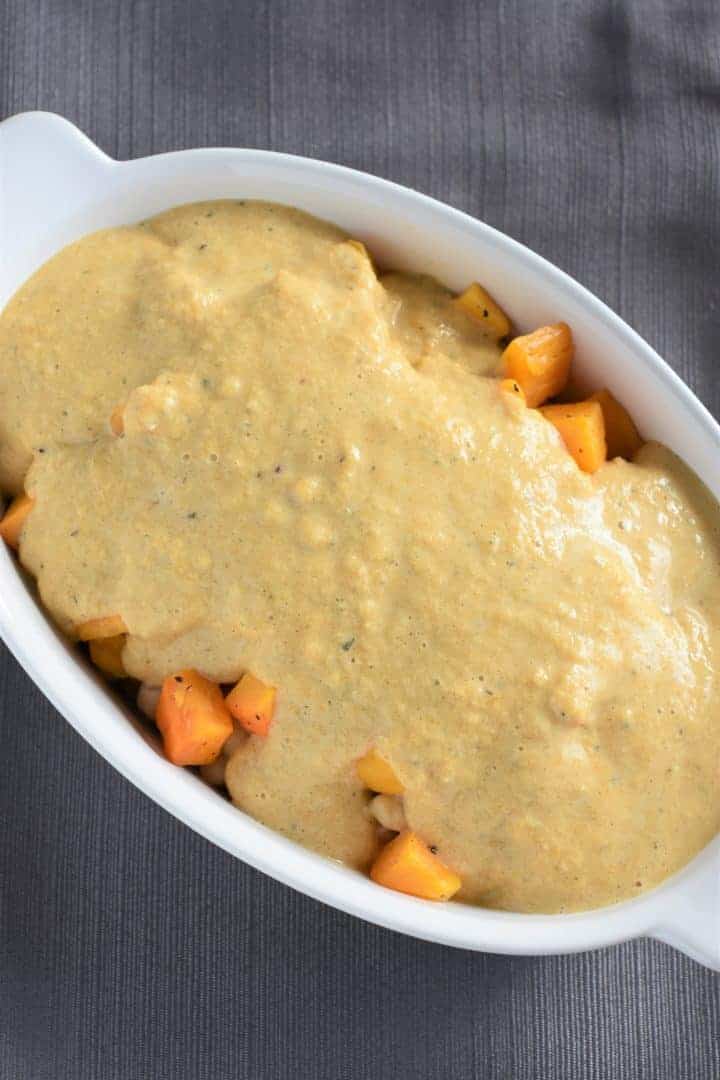 Sauce poured over top of chickpeas and butternut squash in casserole dish