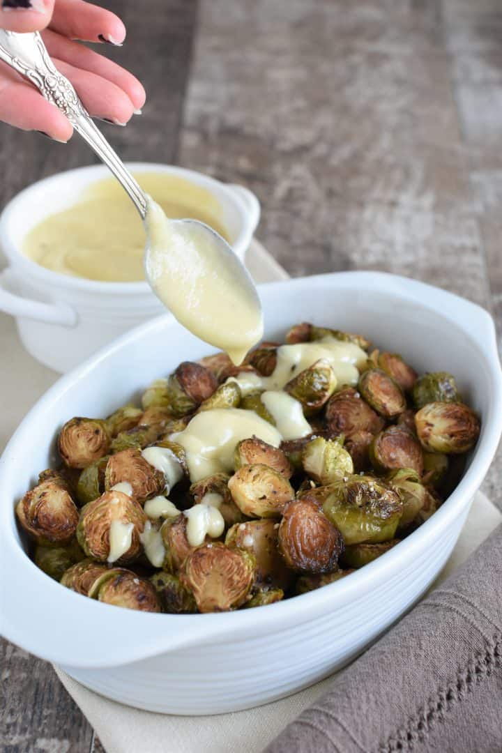 pouring vegan bechamel onto brussels sprouts in a white dish