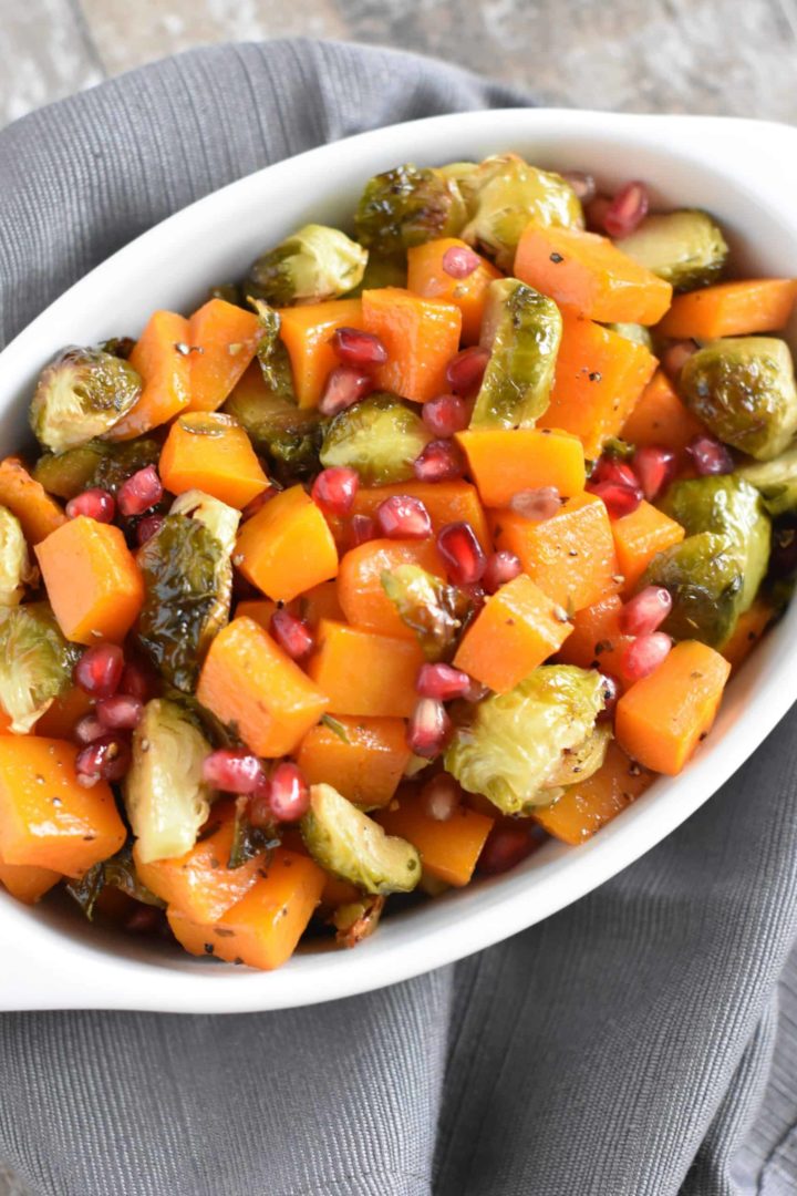 close up of butternut squash and Brussels sprouts with pomegranate arils in white serving dish