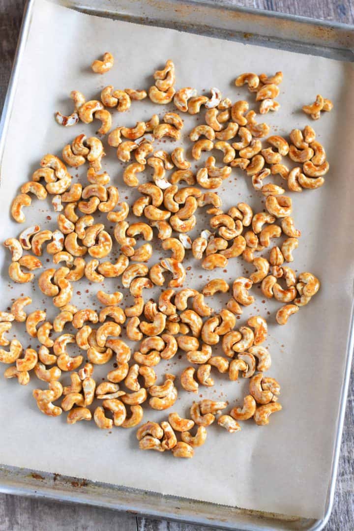 Coasted cashews spread out on a parchment-lined baking sheet