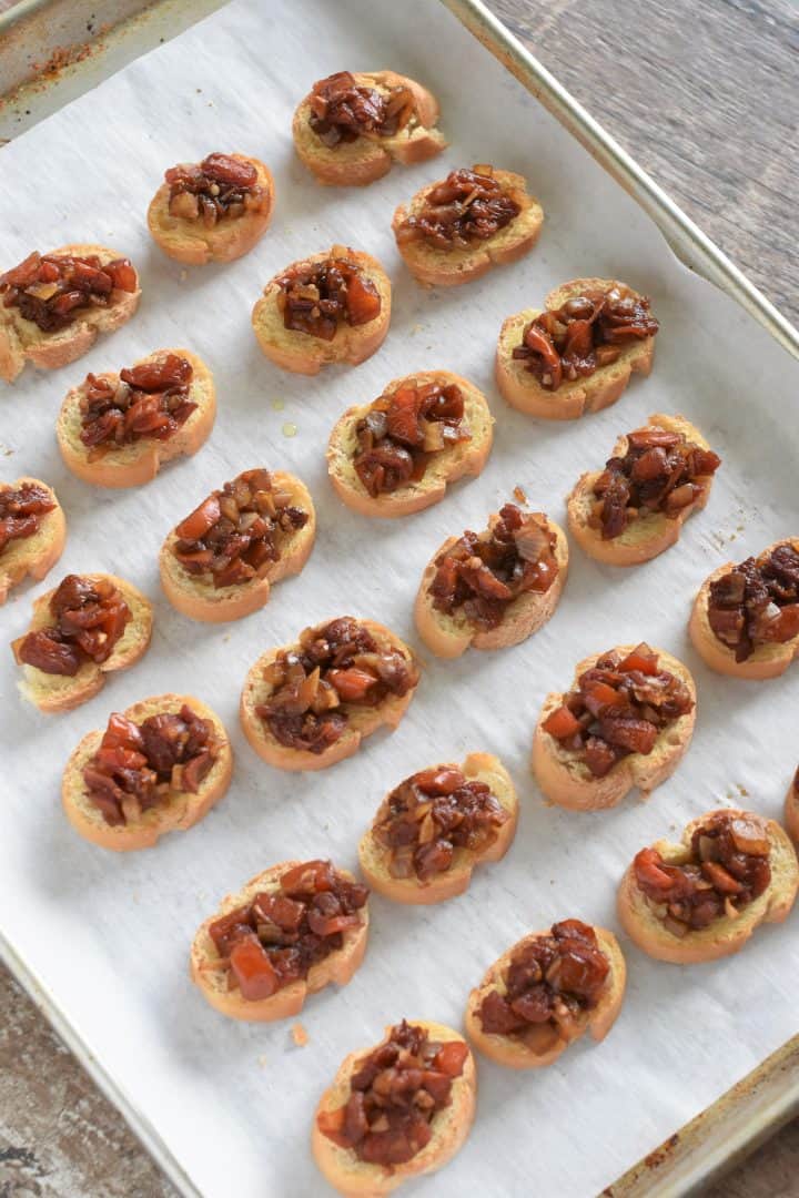 Bread slices topped with tomato mixture on parchment-lined baking sheet