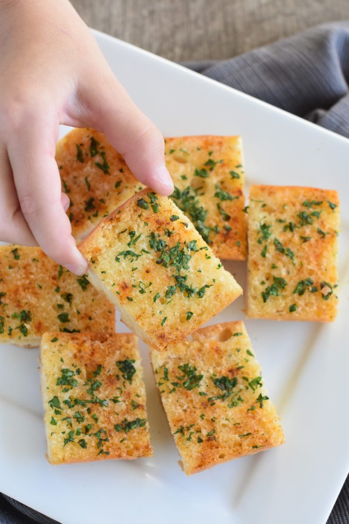Picking up a piece of cut garlic bread from a white plate with more pieces on it