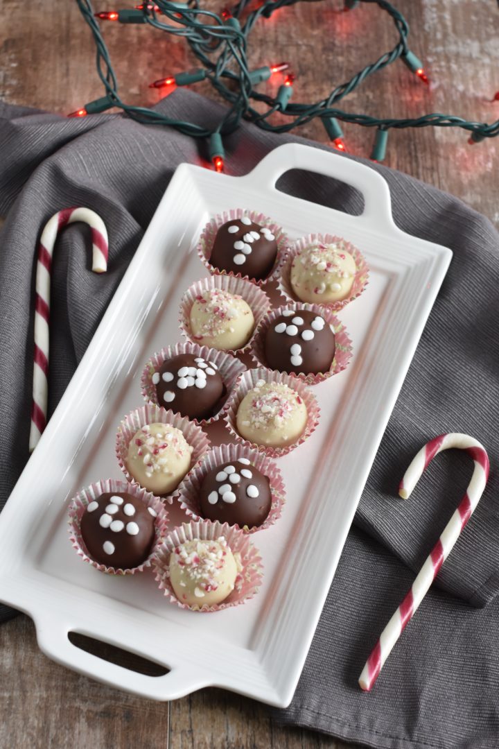 Truffles on white serving platter on kitchen napkin with candy canes next to it and with red Christmas lights in background