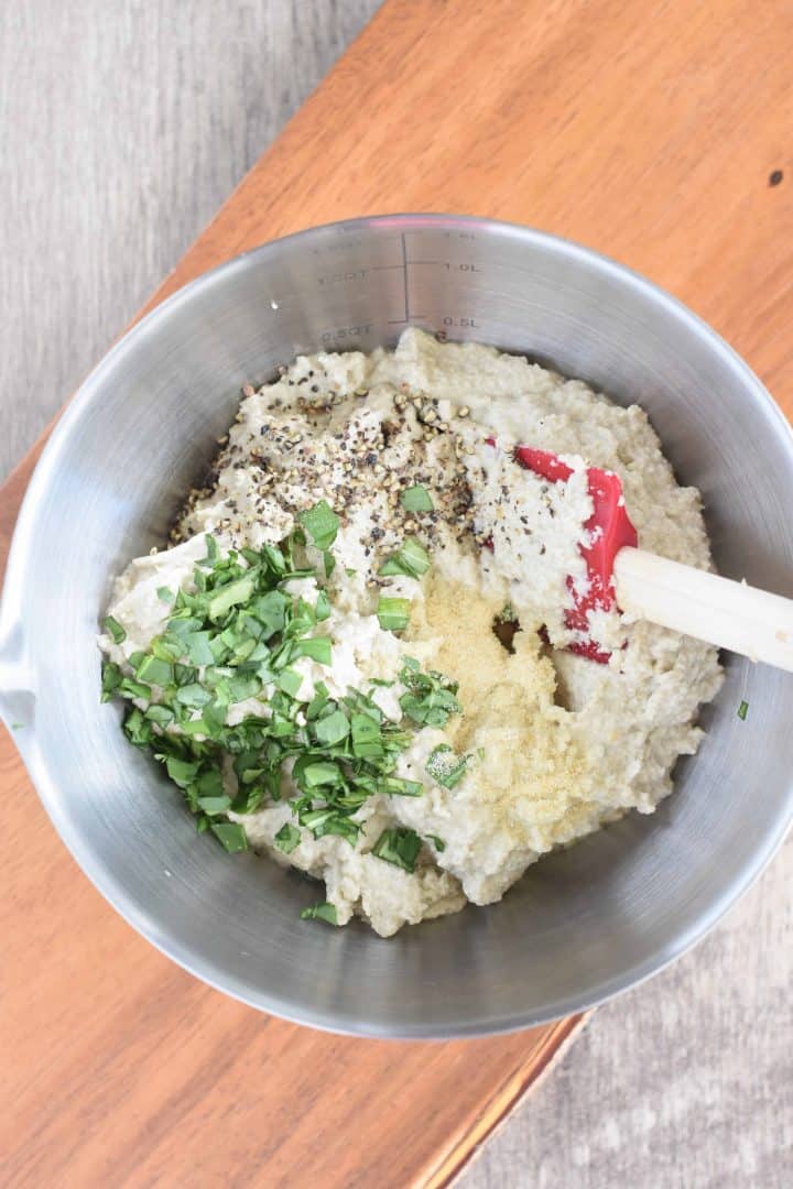 Adding basil, black pepper and garlic powder to sunflower seed ricotta in a mixing bowl