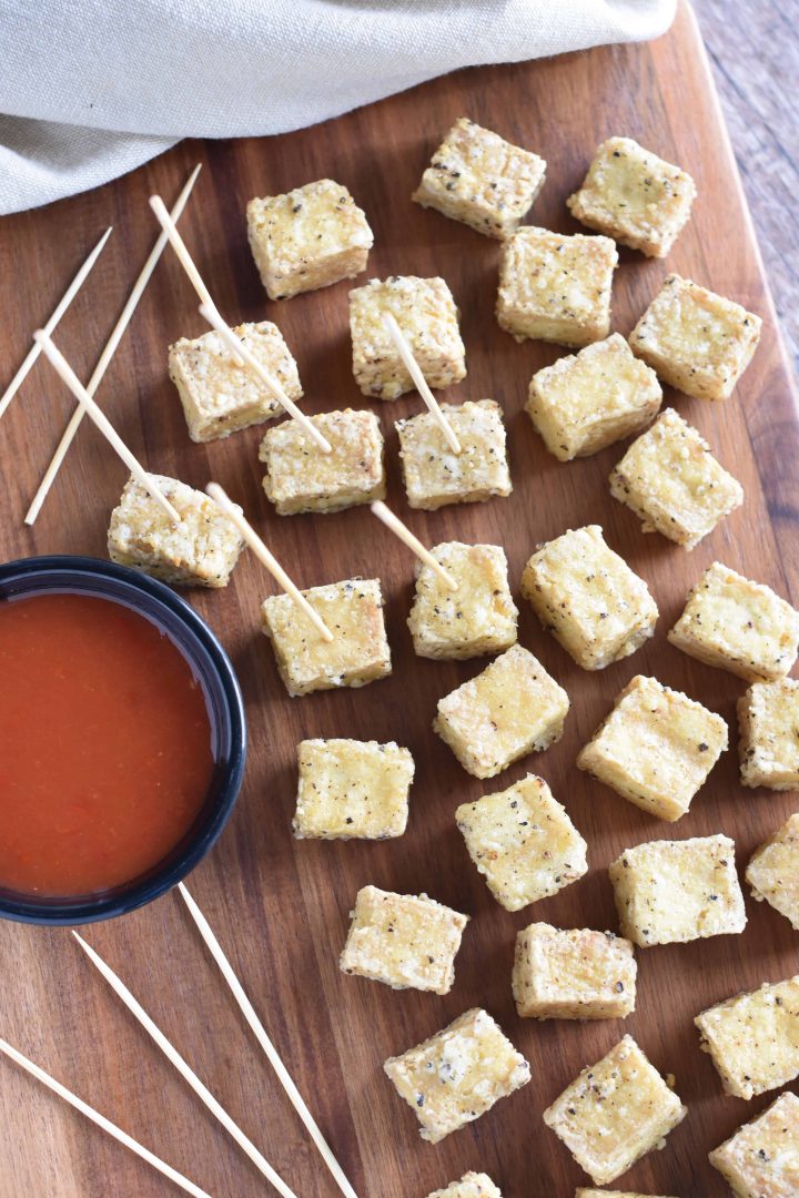 Overhead of tofu on serving block with some serving toothpicks inserted into a few of the pieces