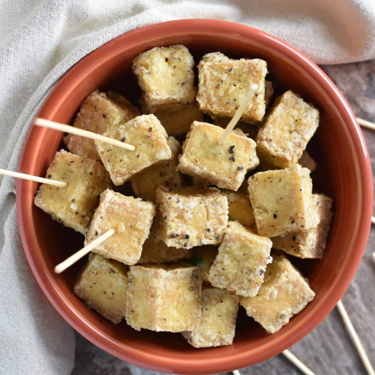 overhead of tofu in a bowl with toothpicks in some of the pieces
