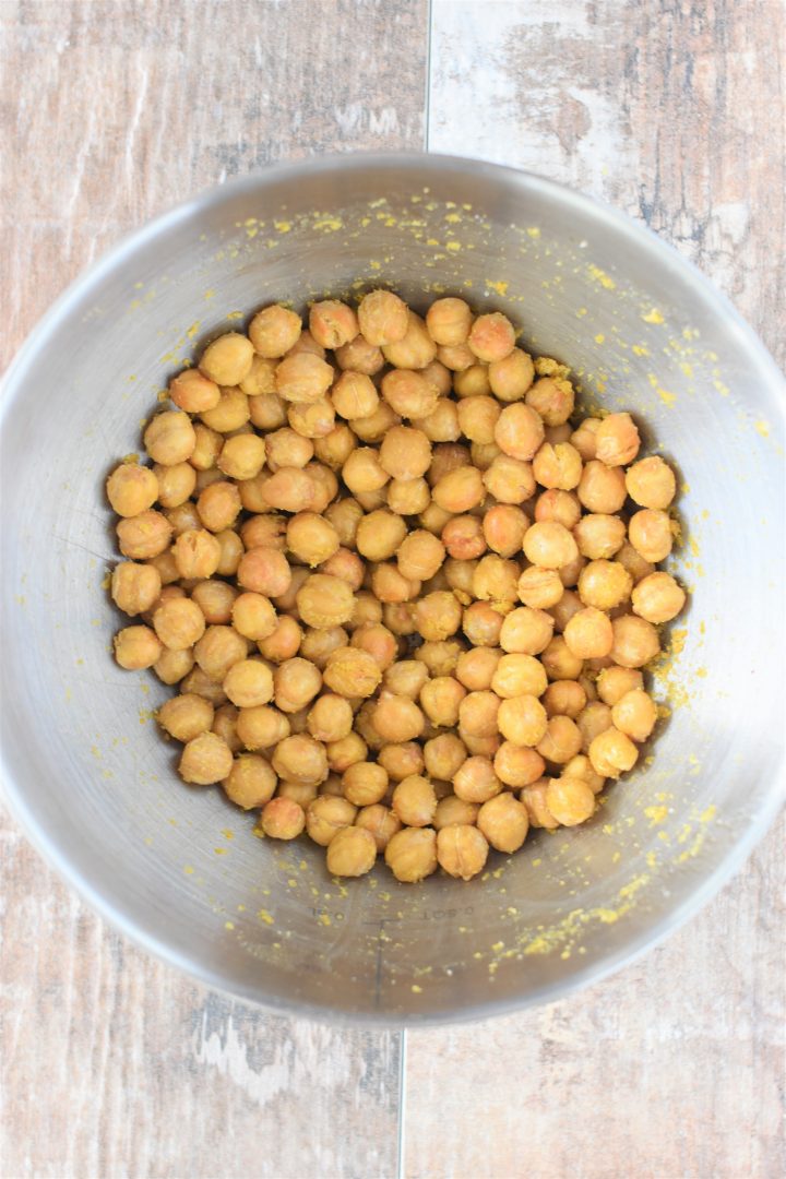 Chickpeas mixed with cheesy seasoning in mixing bowl