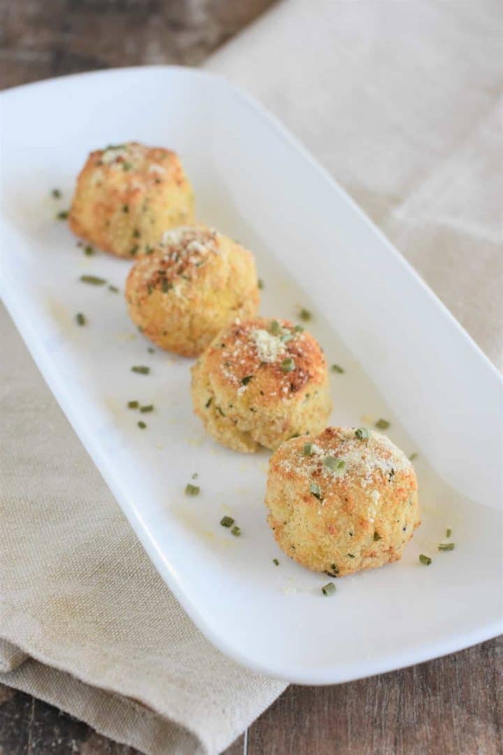 Potato balls on a white serving plate garnished with chives and vegan Parmesan cheese