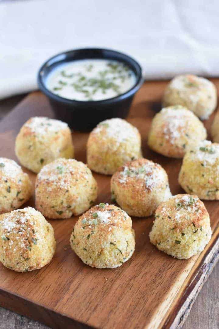 Mashed Potato Balls on a wooden serving block with vegan sour cream and chive dip behind them