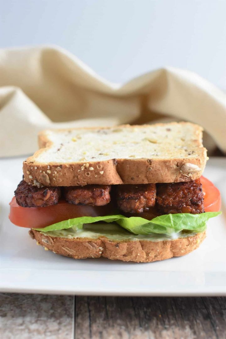 front view of vegan blt sandwich on a white plate with napkin in the background