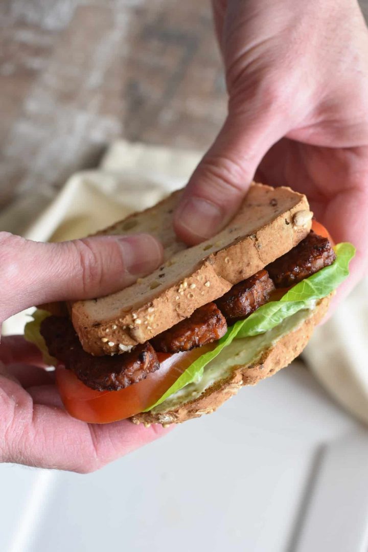 holding a tempeh BLT sandwich over the white plate