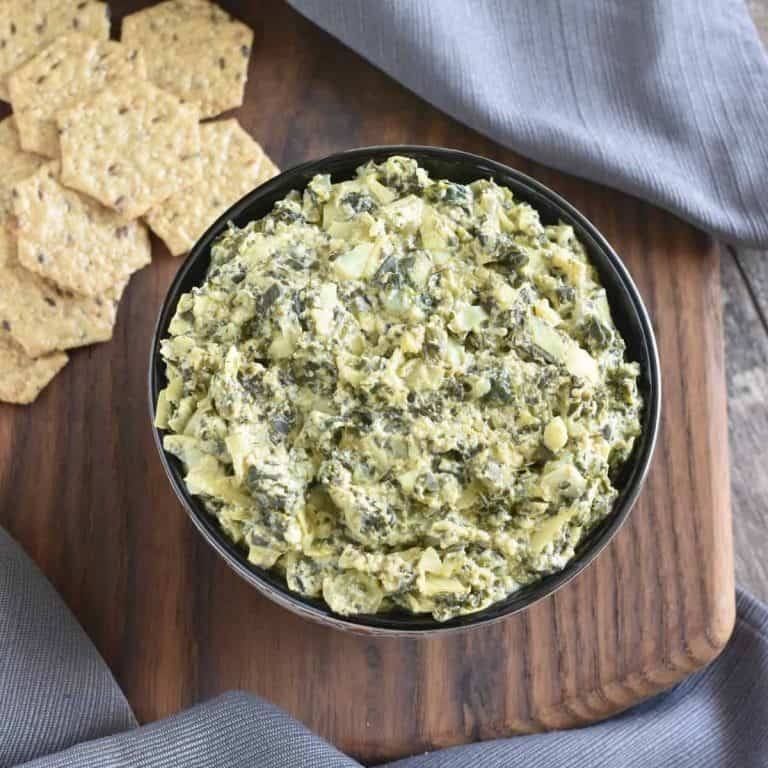 Vegan spinach artichoke dip served in a black bowl with crackers