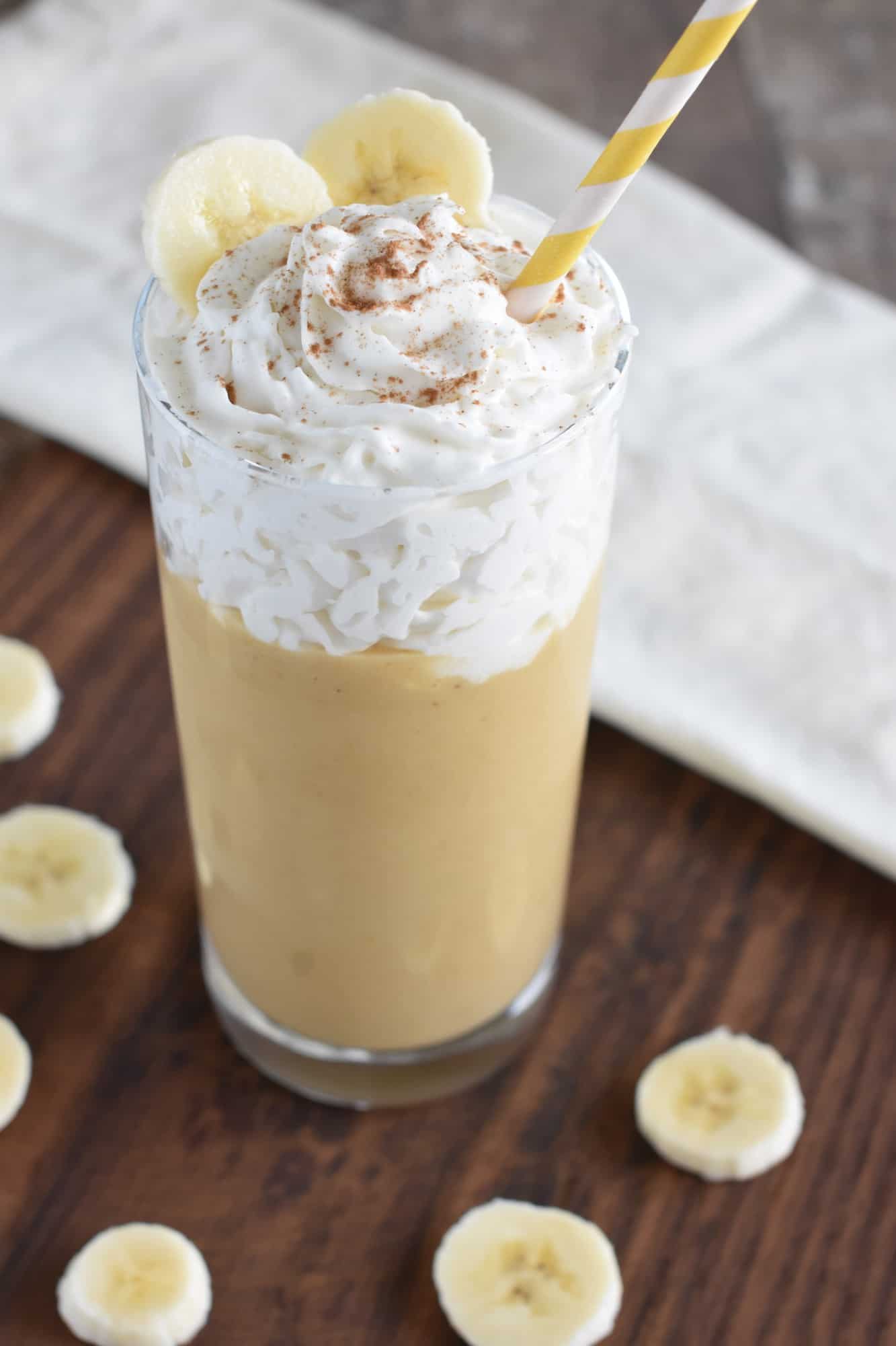 smoothie with non-dairy whipped topping, cinnamon, banana slices and a straw