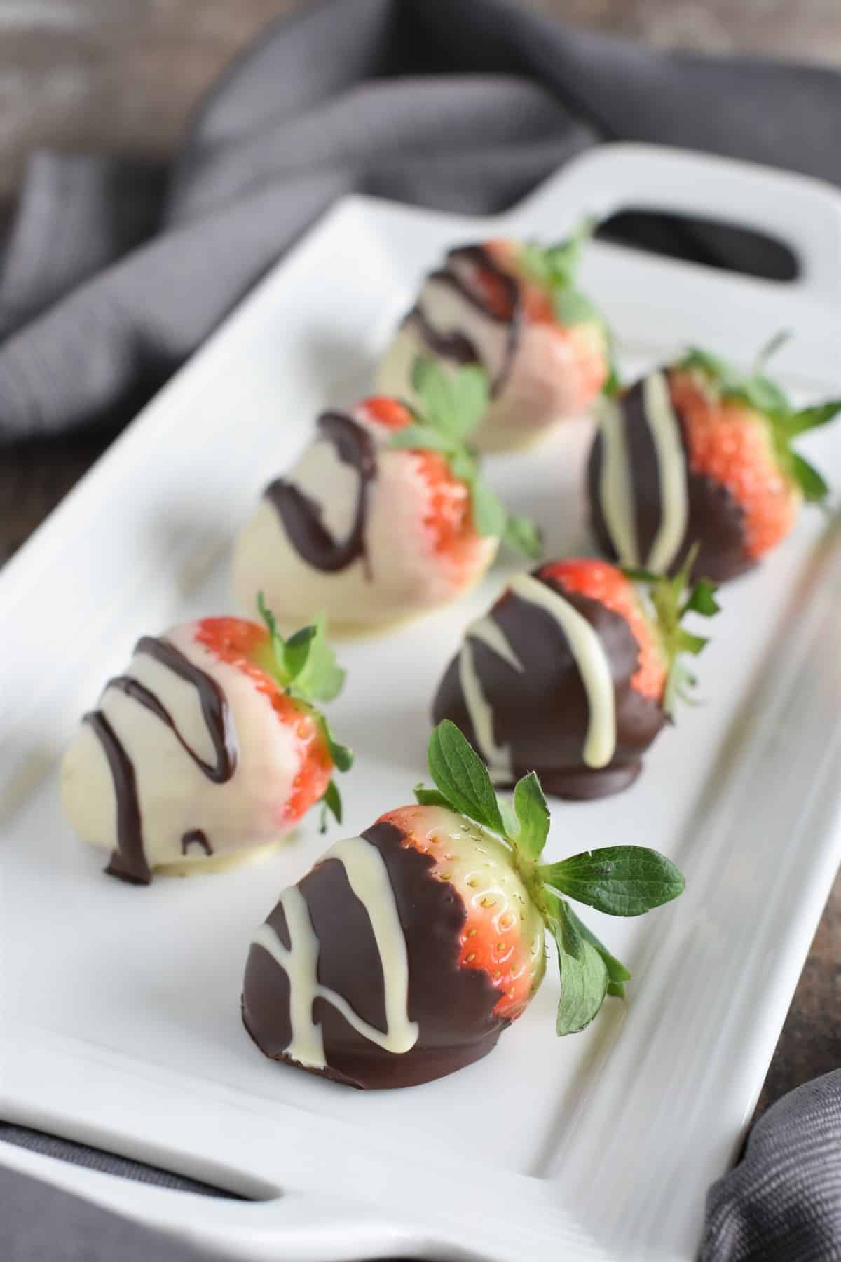 front view of chocolate dipped strawberries on white serving platter
