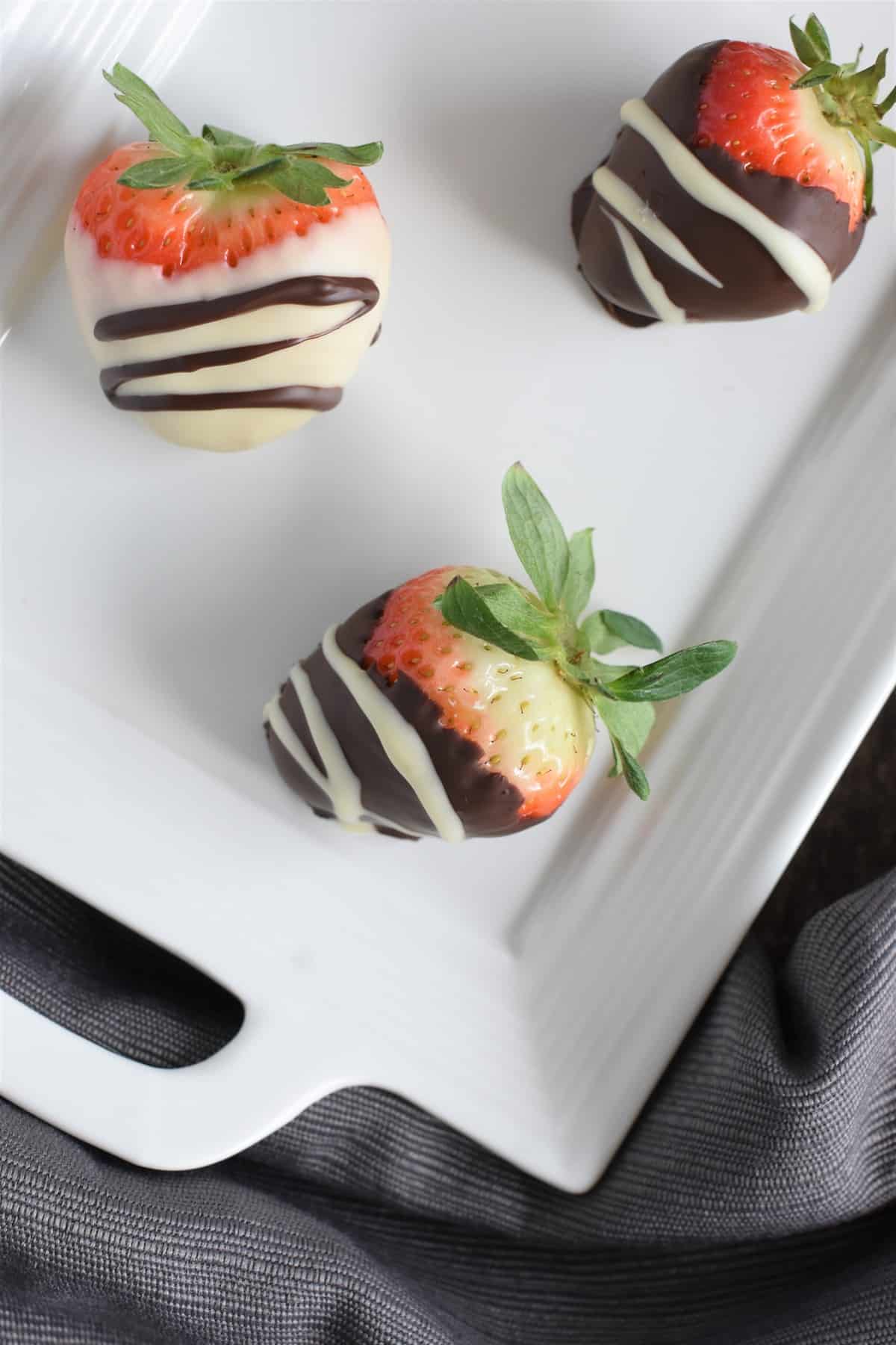 Overhead of three of the chocolate covered strawberries on white platter