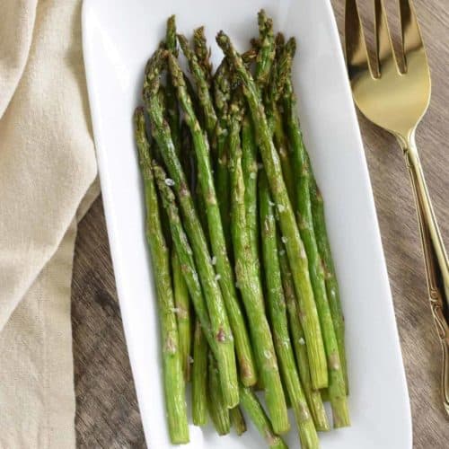 overhead of asparagus on white serving dish with large serving fork next to it