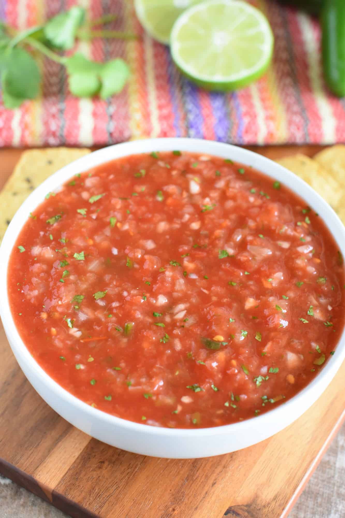 front view of salsa in a white bowl with cilantro, lime and jalapeno in the background