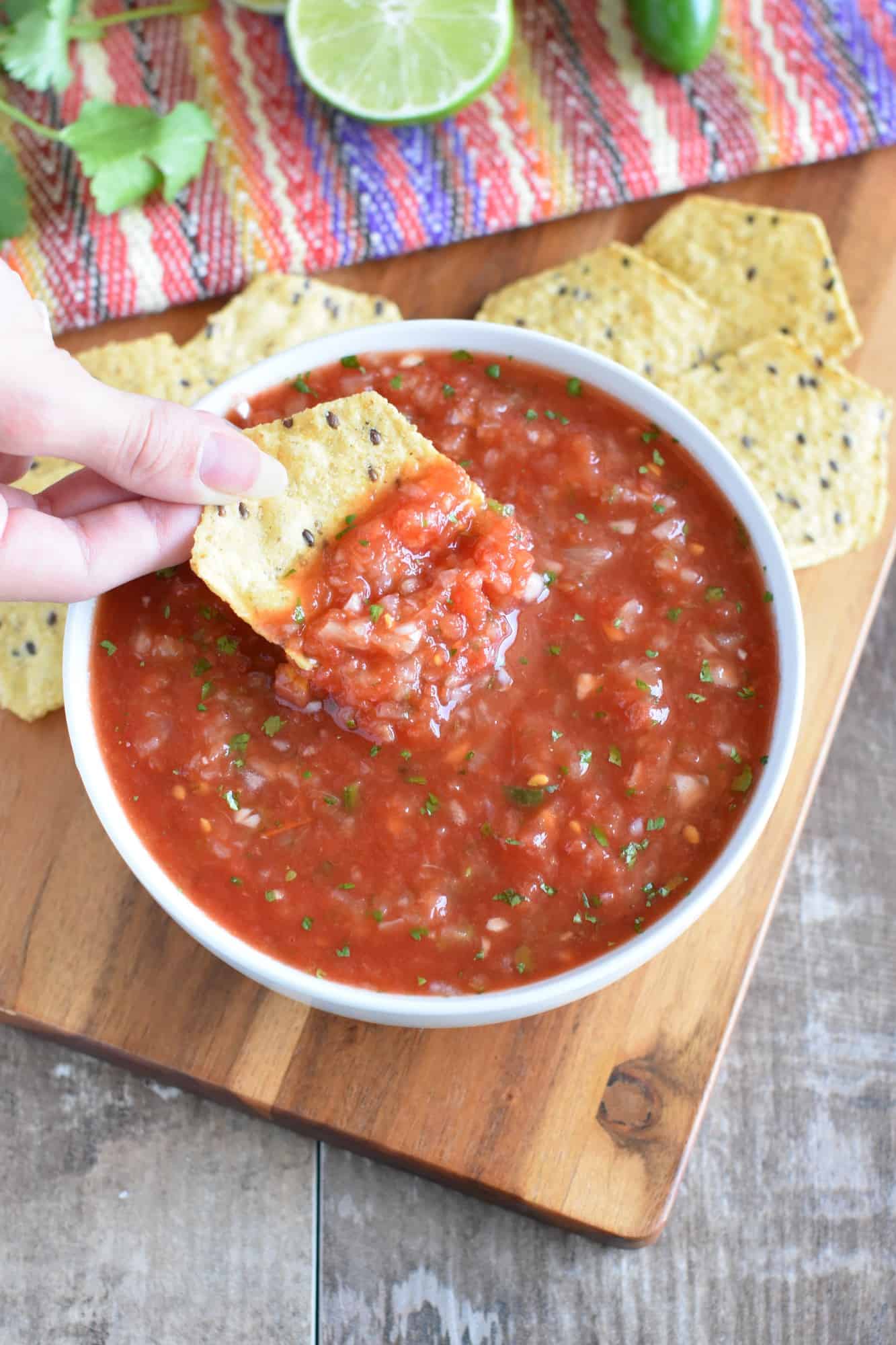 holding a chip with restaurant-style salsa on it over the bowl of the rest of the salsa