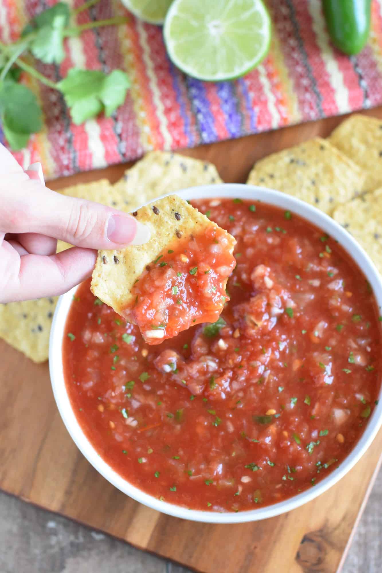 holding a chip with salsa on it over a bowl of salsa