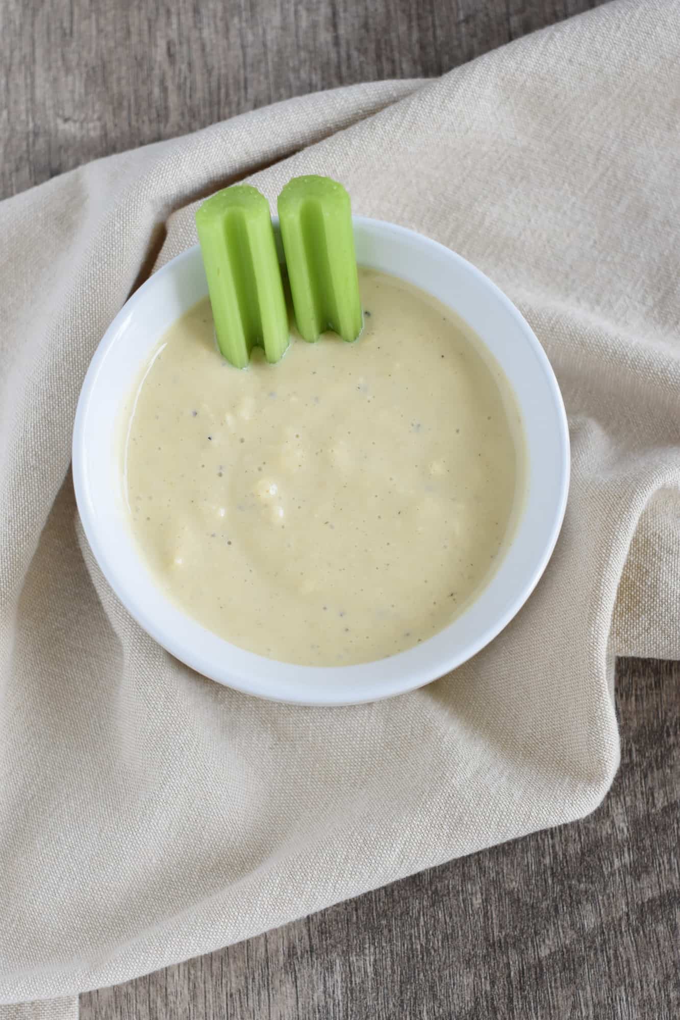 two celery sticks in the dressing in a white serving bowl