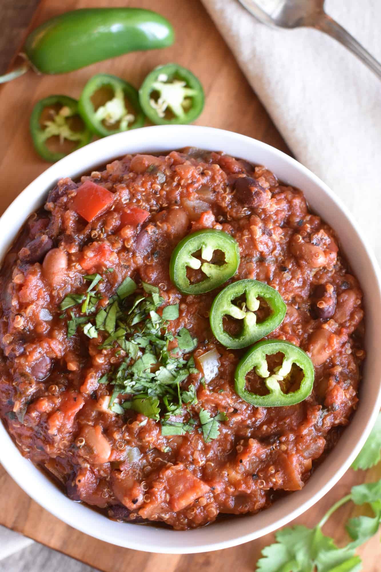 closeup overhead of chili in a white bowl with cilantro and jalapenos on a wooden board
