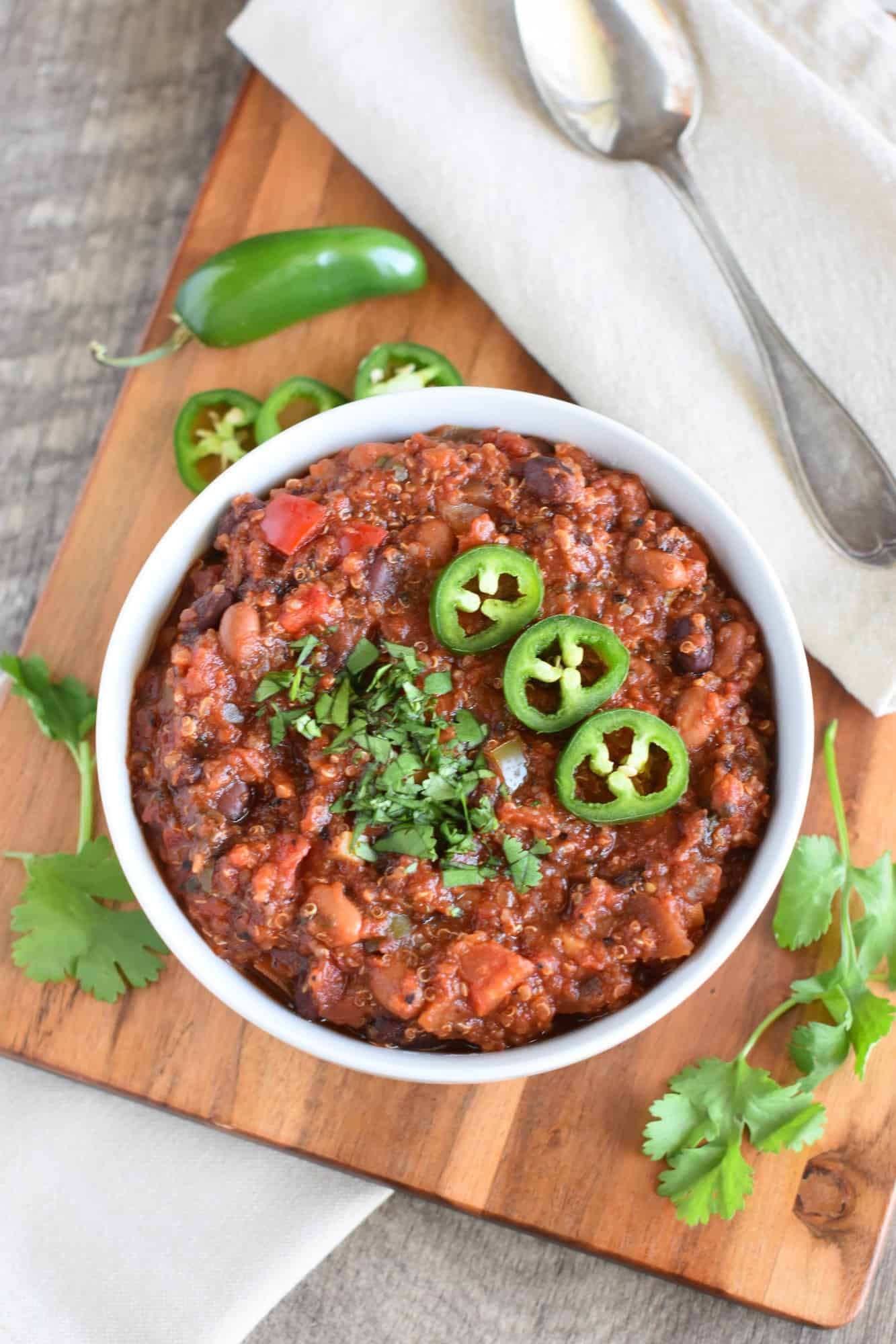 overhead of slow cooker quinoa chili in a white bowl garnished with cilantro and sliced jalapenos