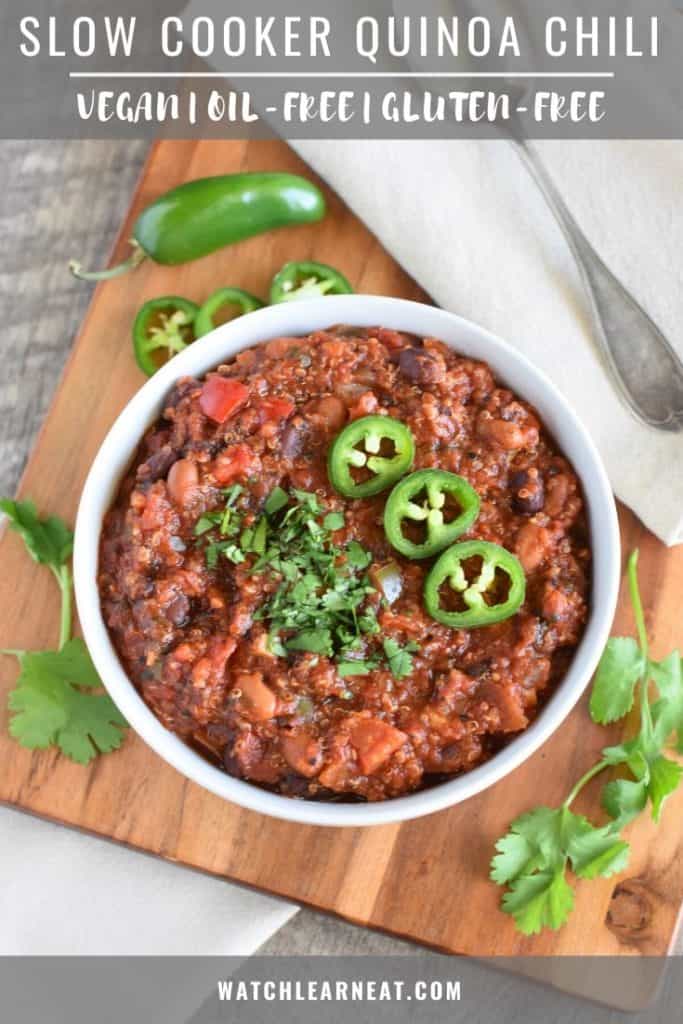 pin of chili in a white bowl on a wooden board with cilantro and jalapeno