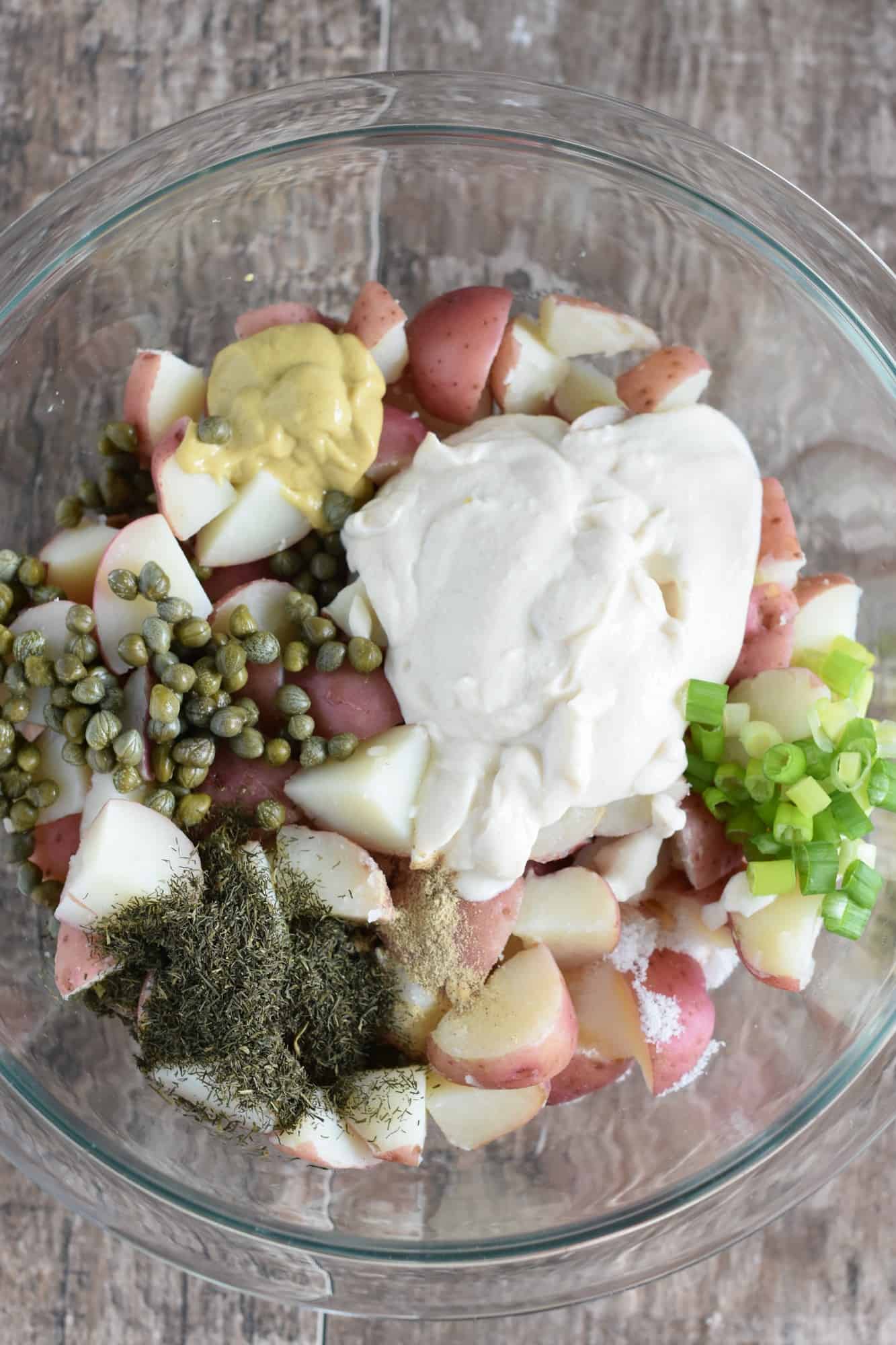 potato salad ingredients added to the potatoes in the glass mixing bowl