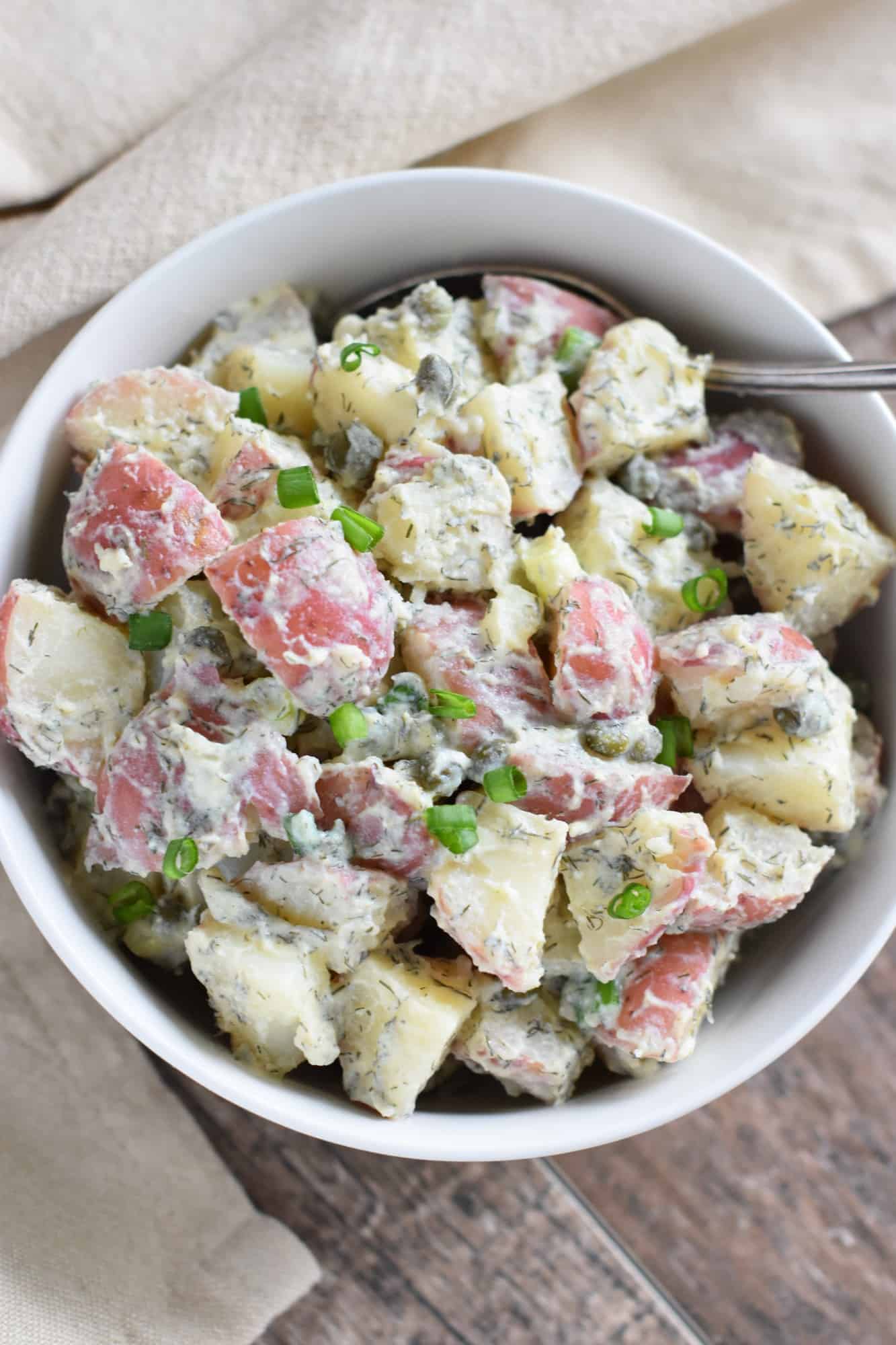 overhead shot of creamy vegan dill potato salad in white bowl with a spoon in it