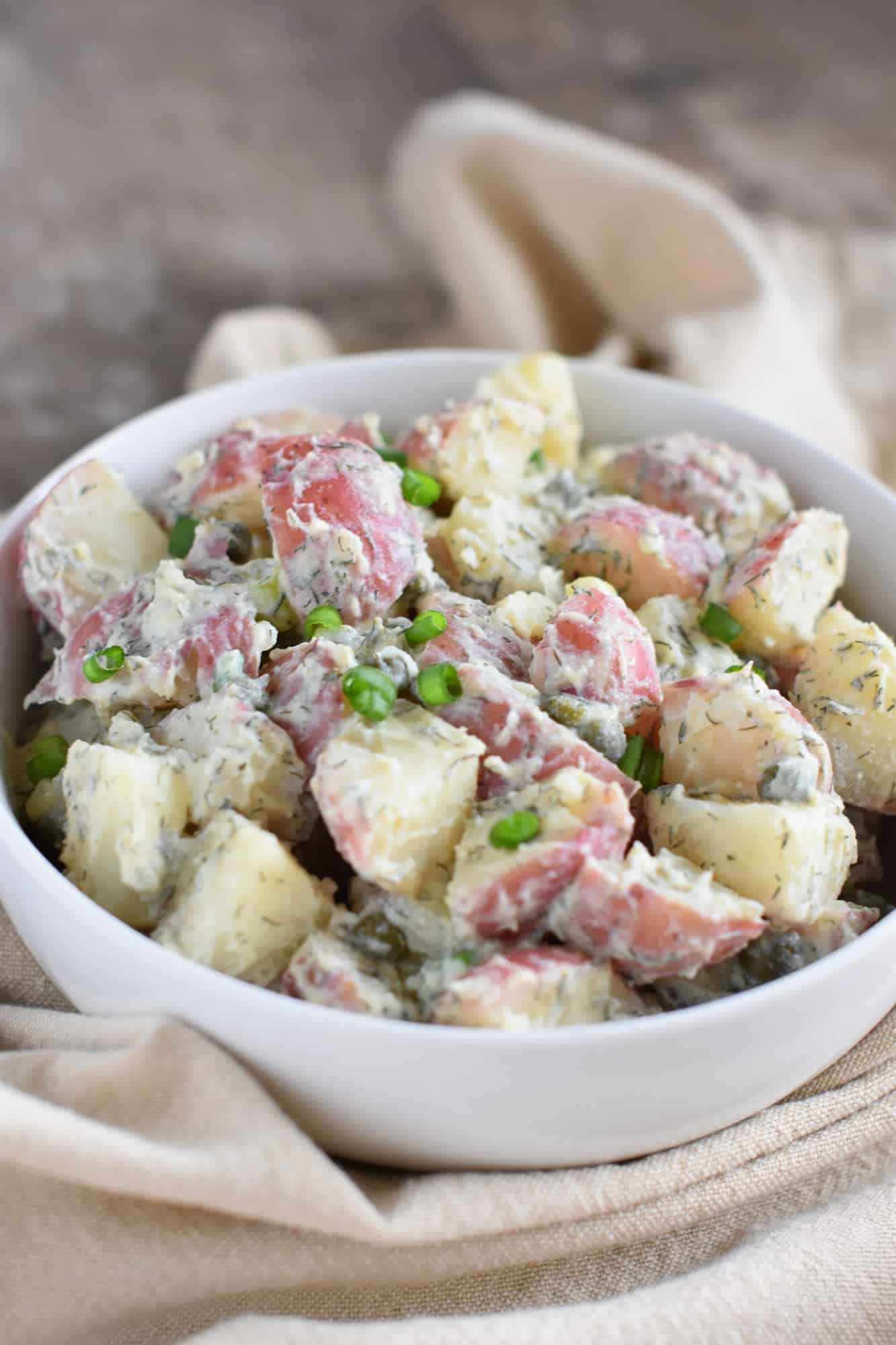 side view of potato salad in white serving bowl on a tan napkin