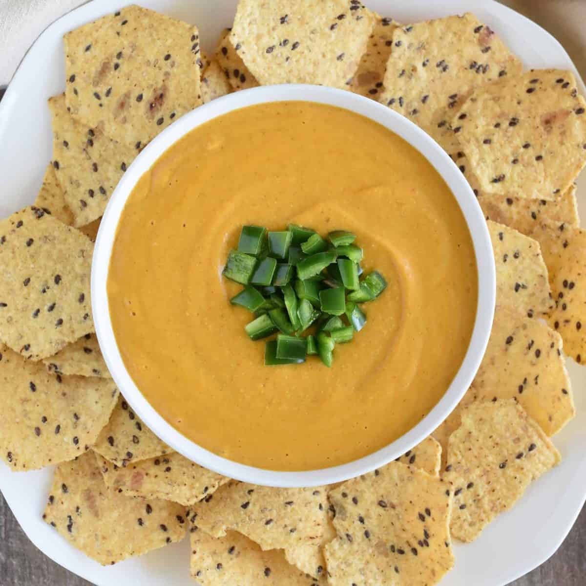 vegan nacho cheese sauce in a white serving bowl with tortilla chips around it on a white platter