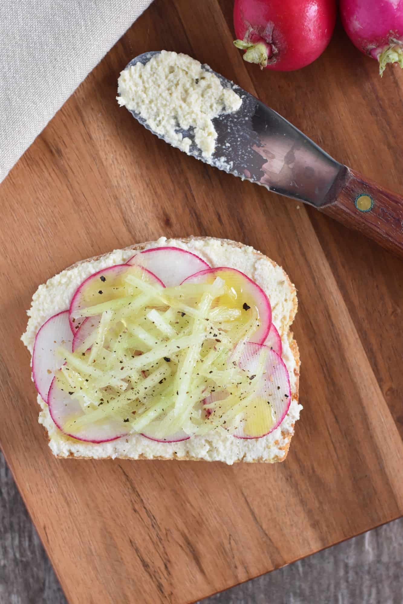 one slice of cucumber and radish ricotta toast on a wooden board