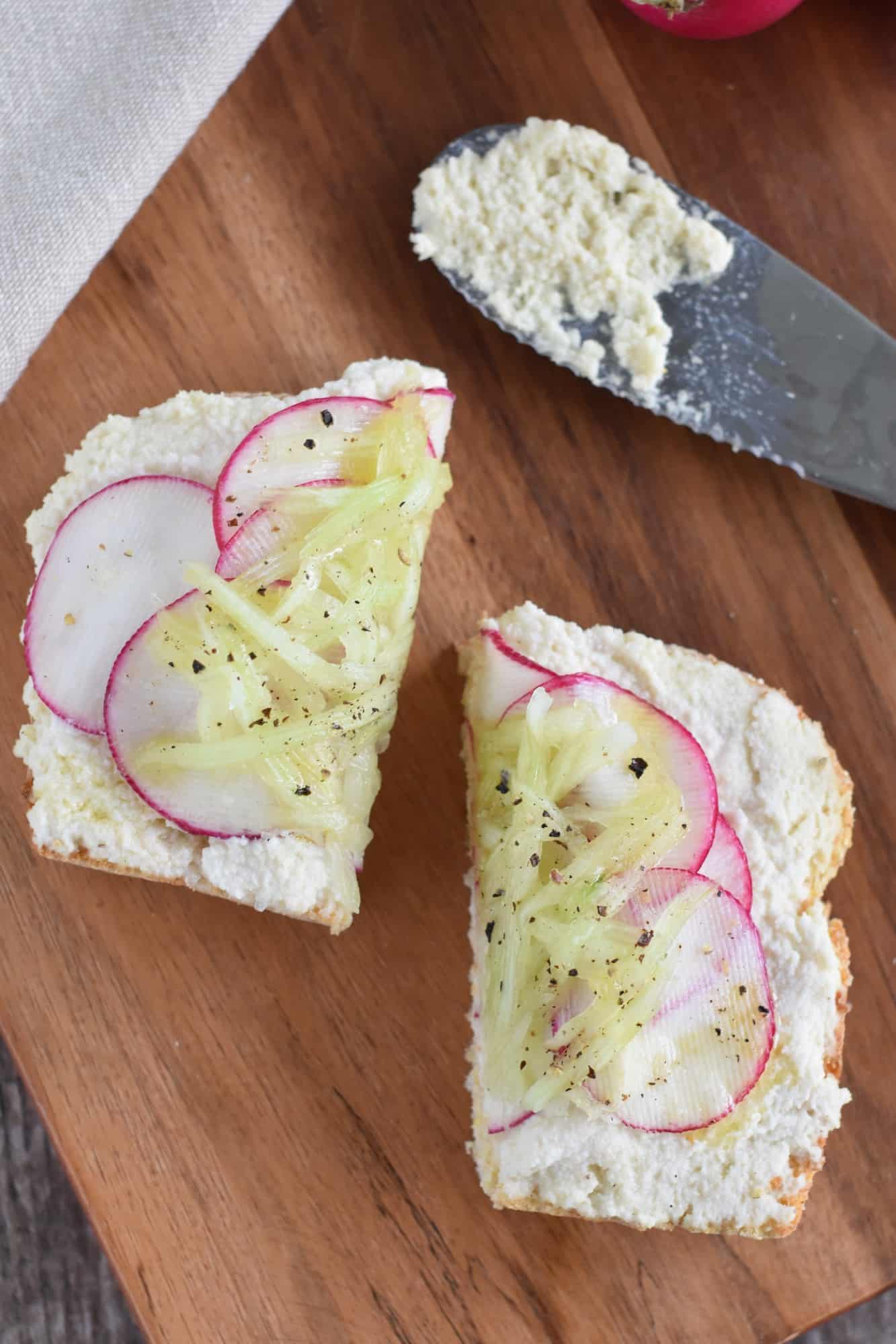 cucumber and radish vegan ricotta toast sliced in half on a wooden board