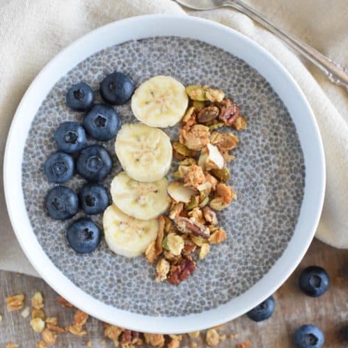 overhead of pudding in a white bowl topped with blueberries, bananas and granola