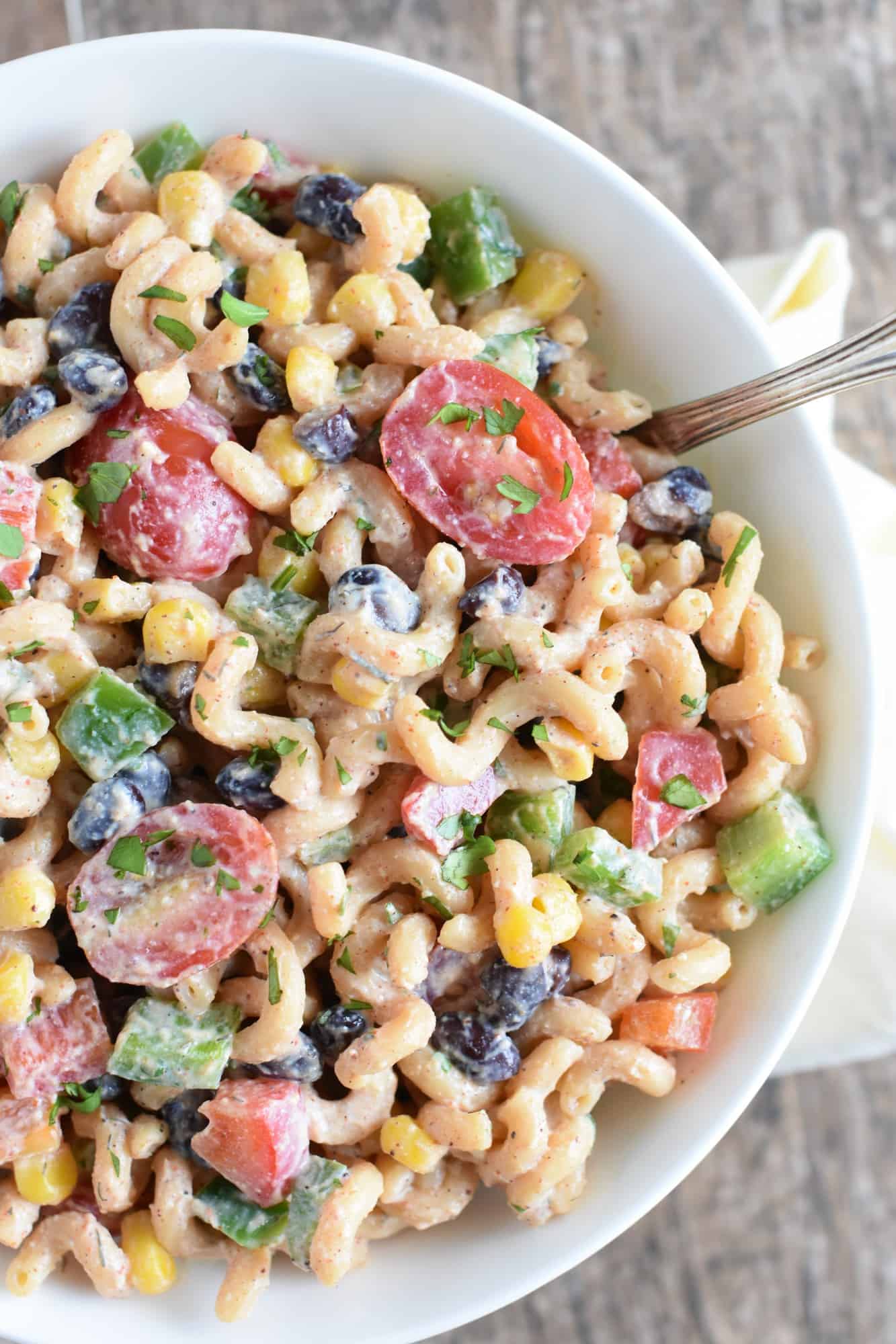 overhead close up of southwest lentil pasta salad in a white bowl with a spoon in it