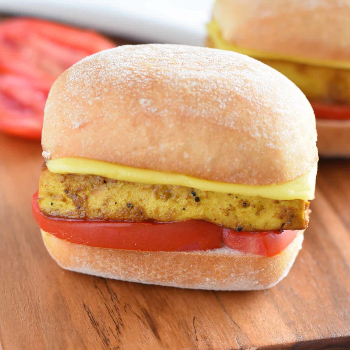 front view of a vegan egg and cheese sandwich on a wooden board with another in the background