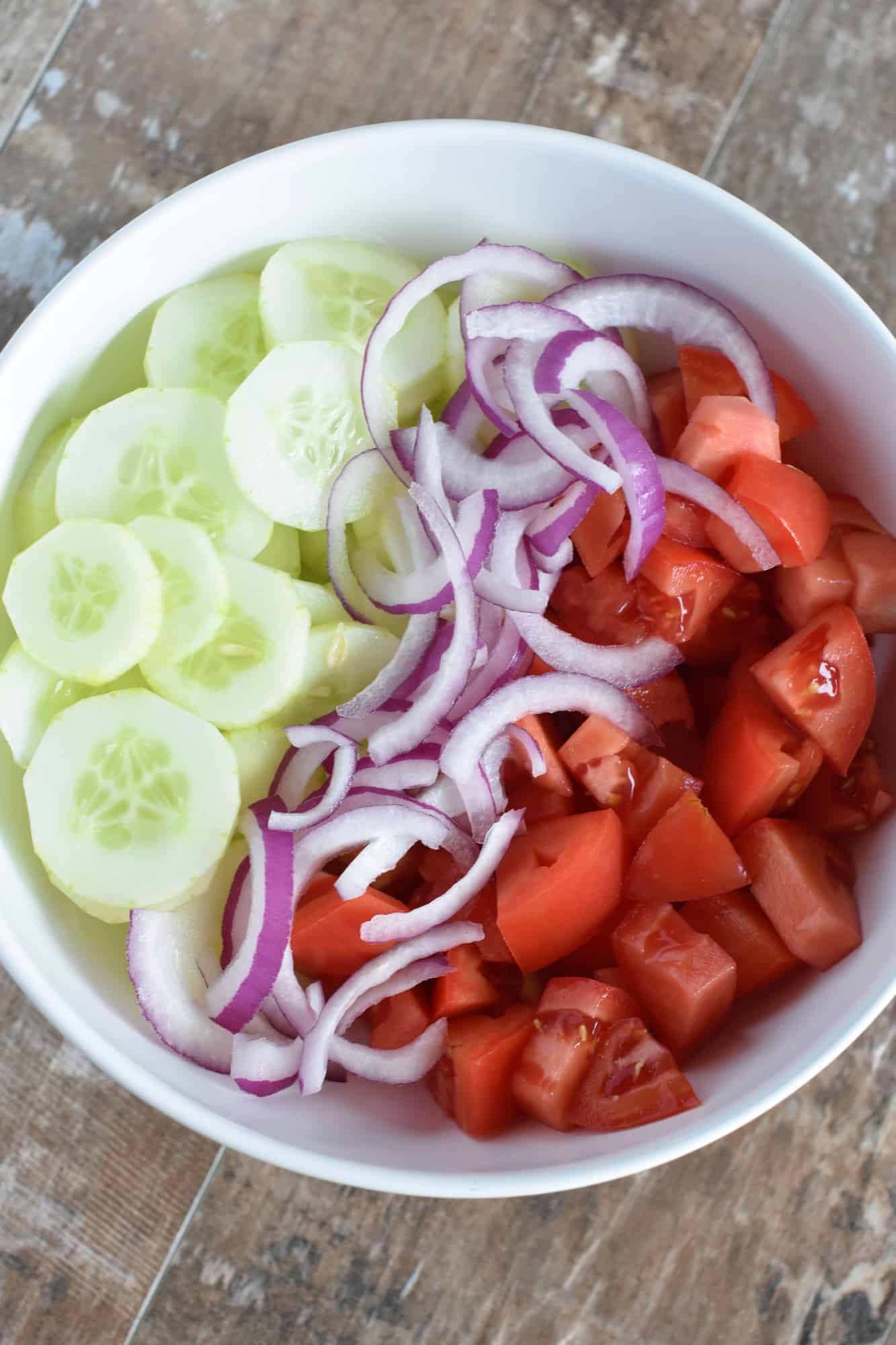 tomatoes, onion and cucumbers added to a mixing bowl