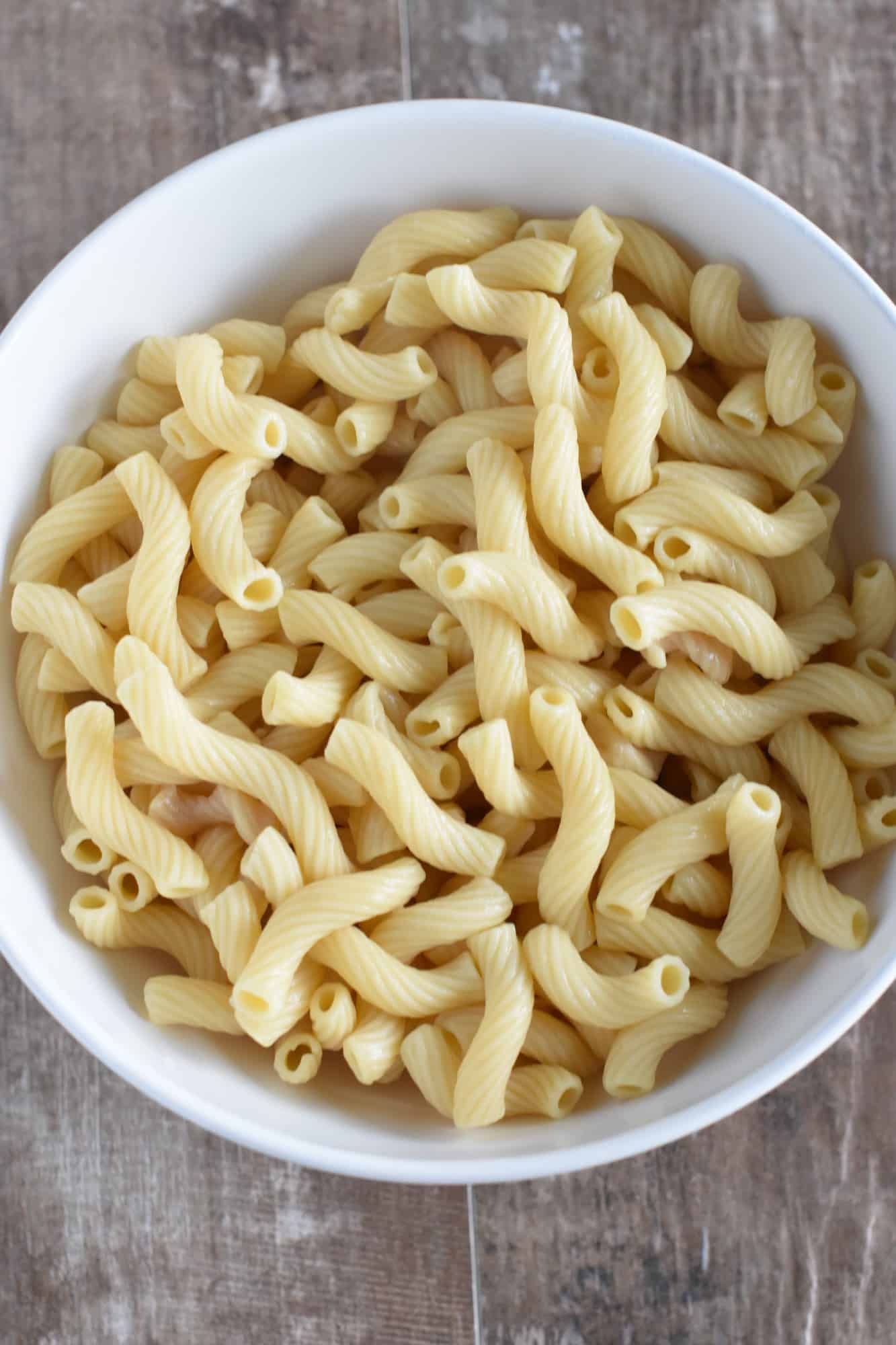 cooked pasta added to a large white serving bowl