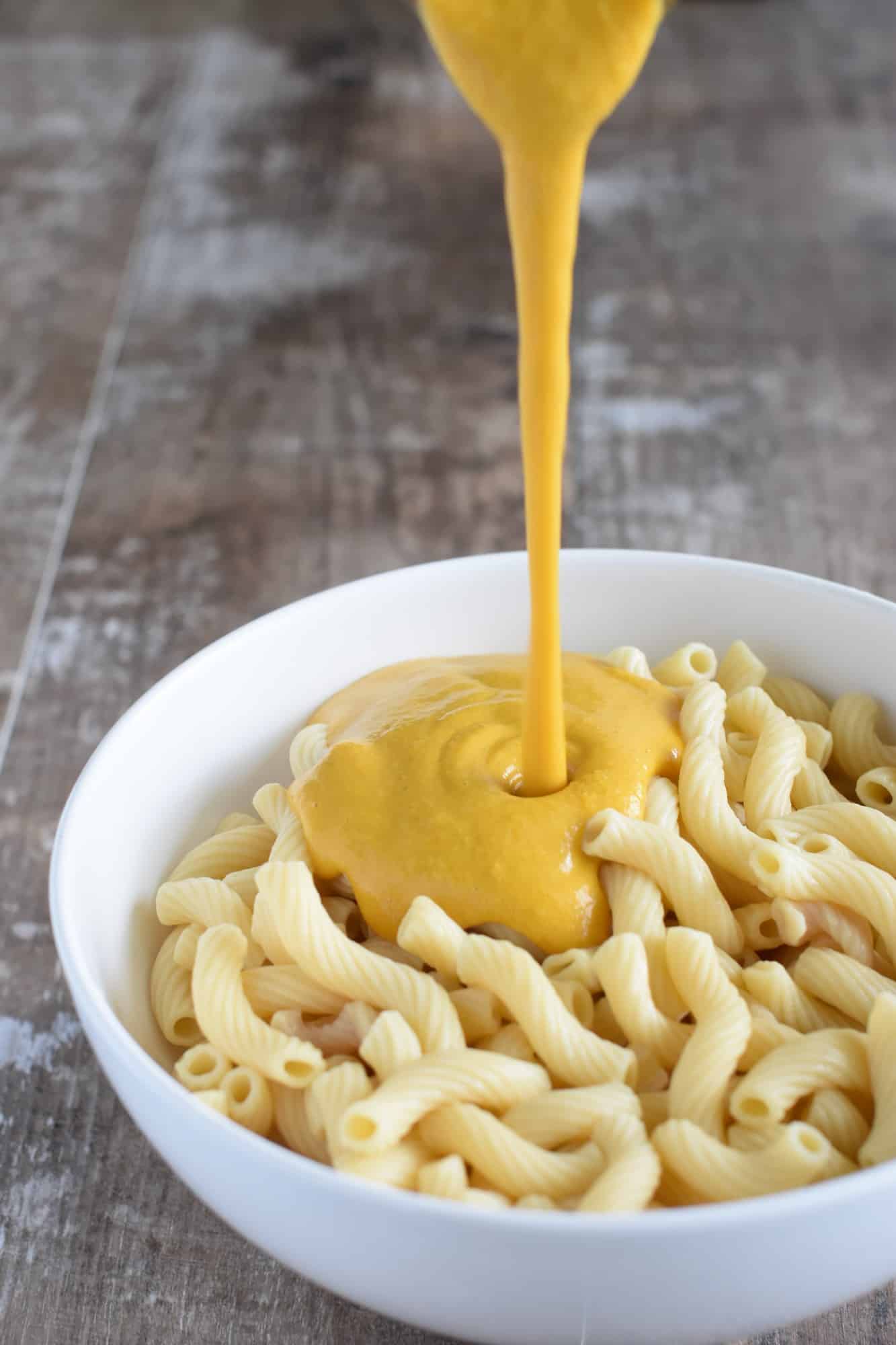 pouring the cheese sauce onto the pasta in the serving bowl