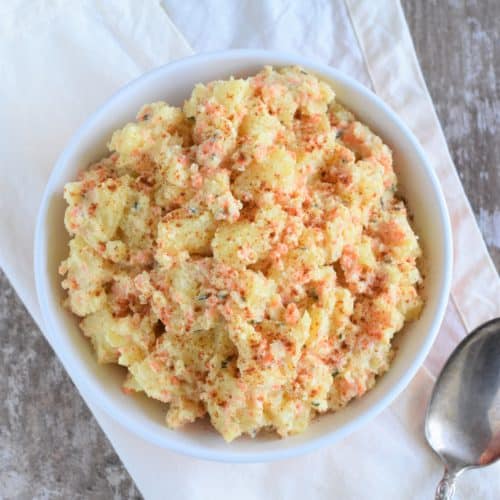 overhead of potato salad in a bowl on a kitchen napkin with a spoon next to it