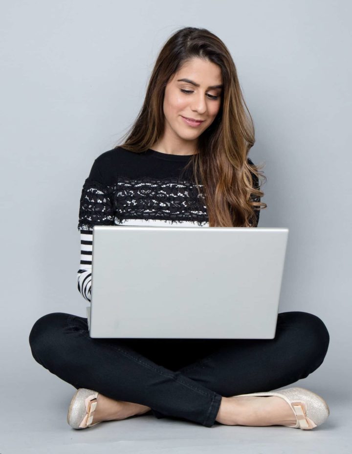 woman smiling as she sits with her legs crossed and works on her laptop