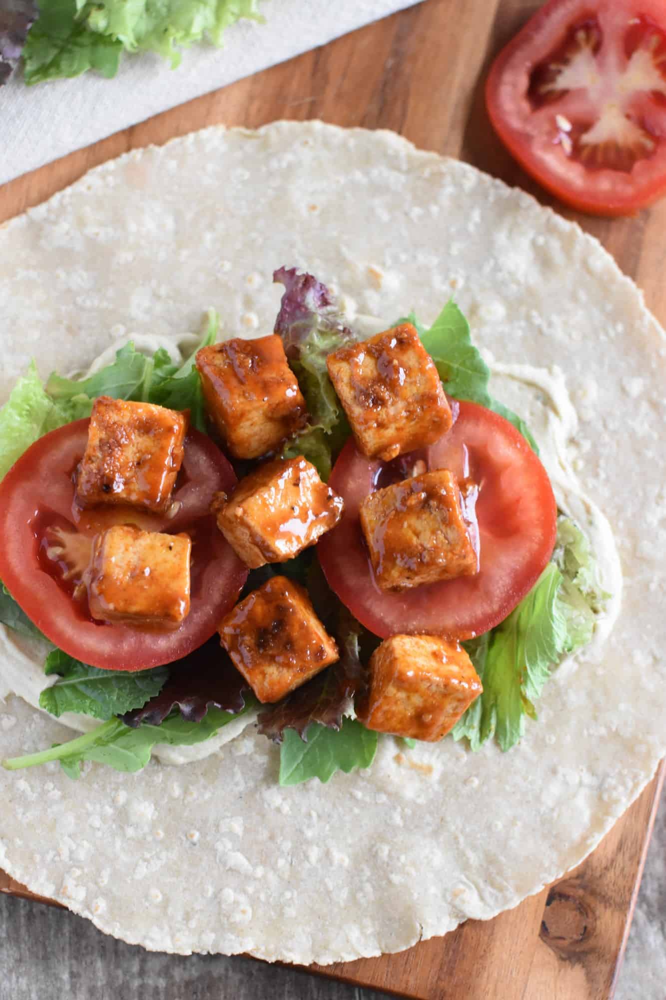 tofu in a wrap with hummus, greens and tomatoes