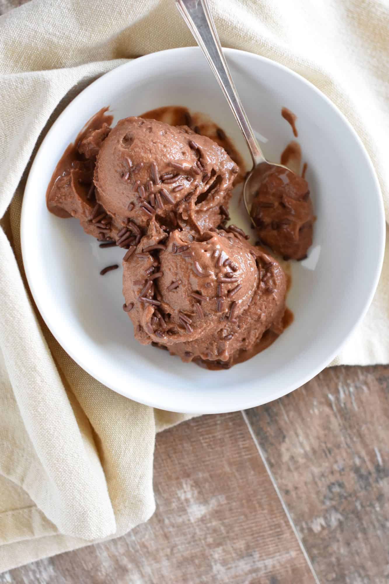 overhead of chocolate nice cream in a white bowl with some sprinkles and a spoon