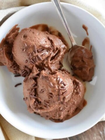 two scoops chocolate nice cream with chocolate sprinkles in a white bowl with a spoon on the side