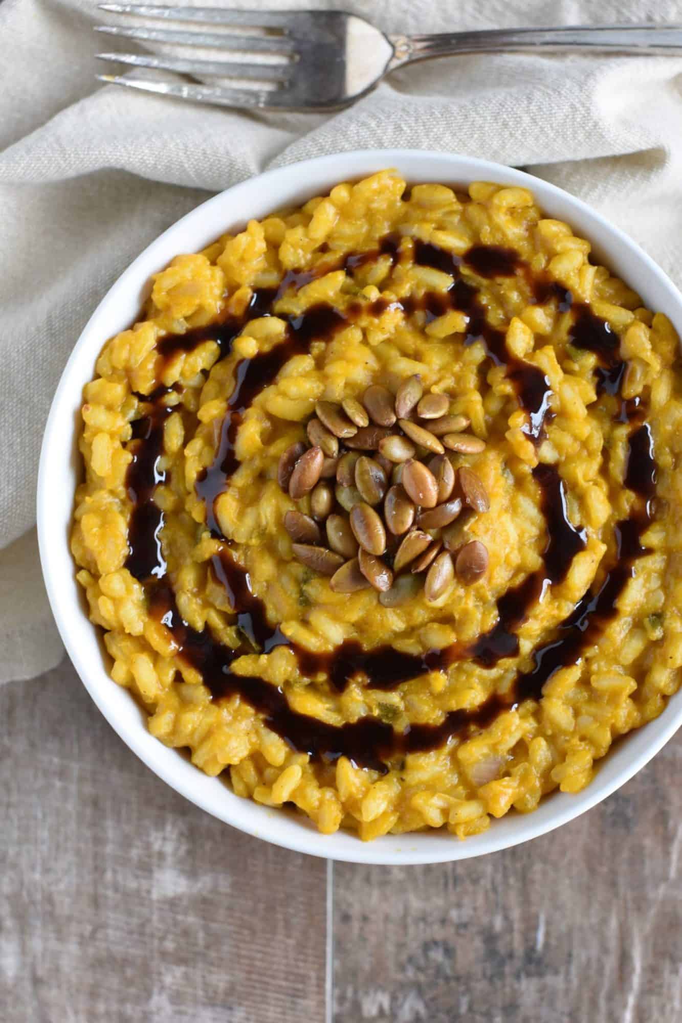 overhead of vegan pumpkin risotto in a white bowl with roasted pepitas and balsamic glaze.