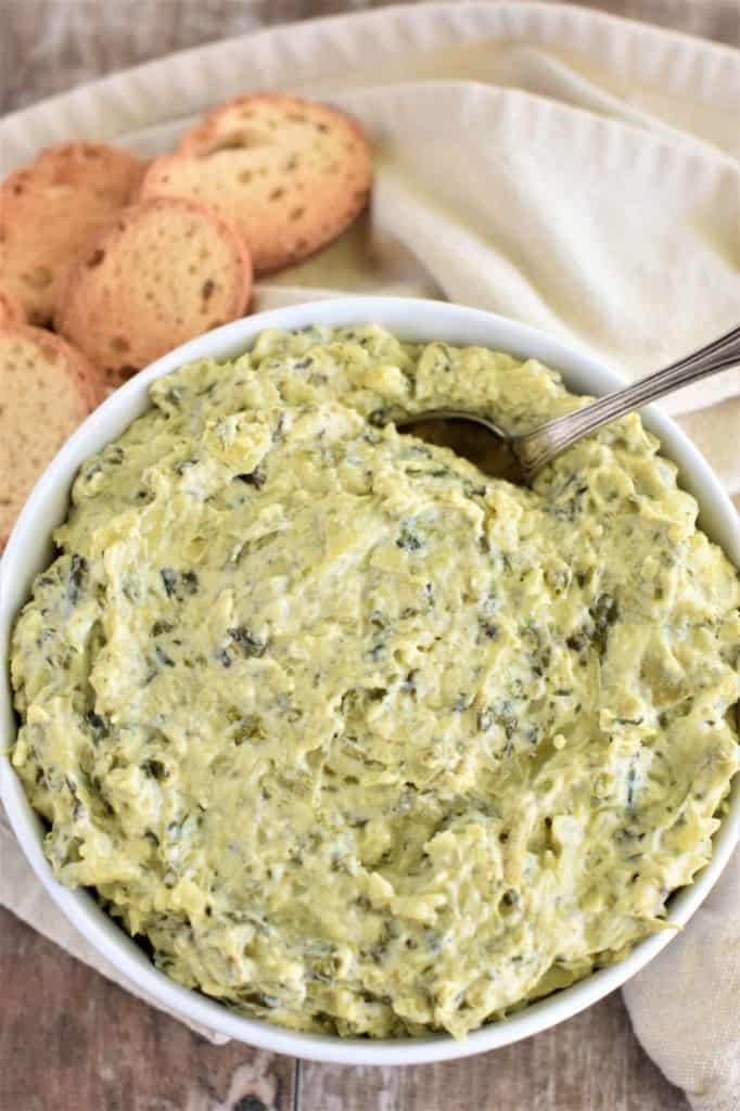 overhead of dip in a white bowl with a spoon in it and some bread slices behind it