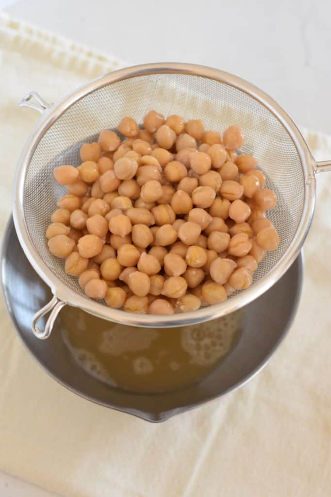 holding a mesh strainer of chickpeas over a mixing bowl