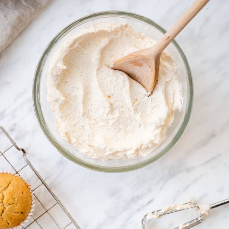 overhead of frosting in mixing bowl with wooden spoon in it